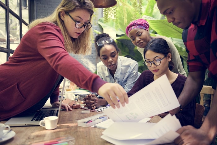 A group of employees bend over a desk at their workspace, reviewing documents.