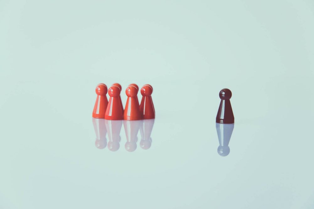 A group of red pawns with a black one standing separately, symbolising managers.