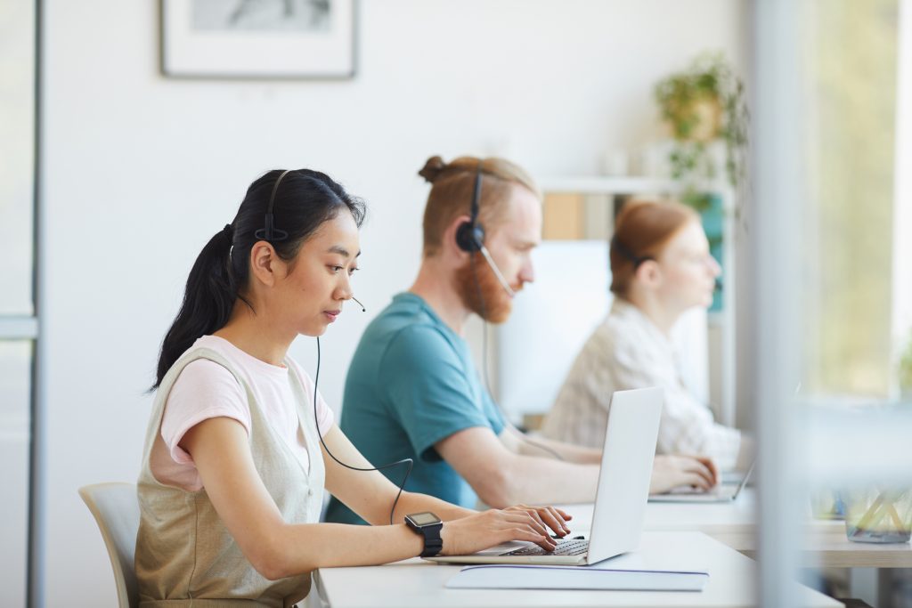 Three people working side by side on laptops with headsets